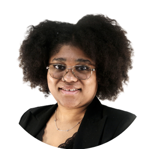 Portrait of a smiling woman with curly hair, wearing glasses and a black blazer, accessorized with a delicate necklace.